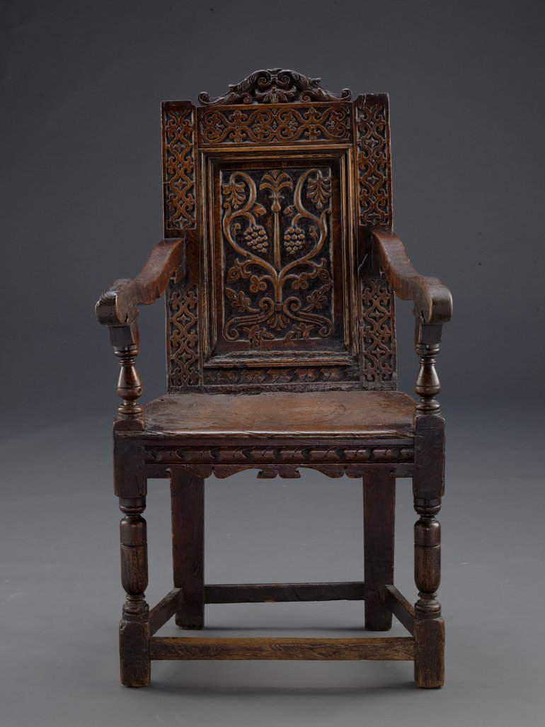 The carved oak Bidford Chair photographed against a grey studio background.